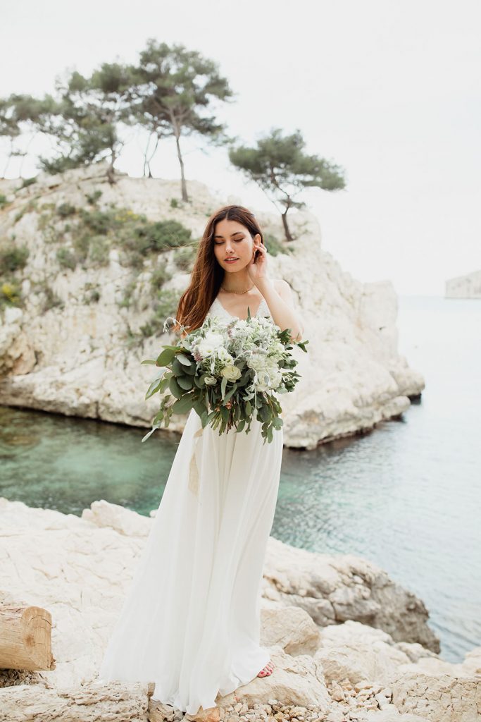 Château Grand Boise Provence wedding bride portrait with sea view Bride holding bouquet at Château Grand Boise Provence wedding venue overlooking Mediterranean cliffs and vineyard landscape by photographer Maxime Bernadin