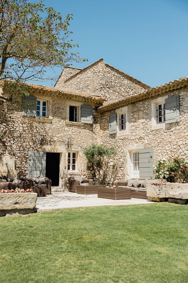 Rustic stone villa with blue shutters and courtyard seating at Mas de la Rose, captured by Maxime Bernadin.
