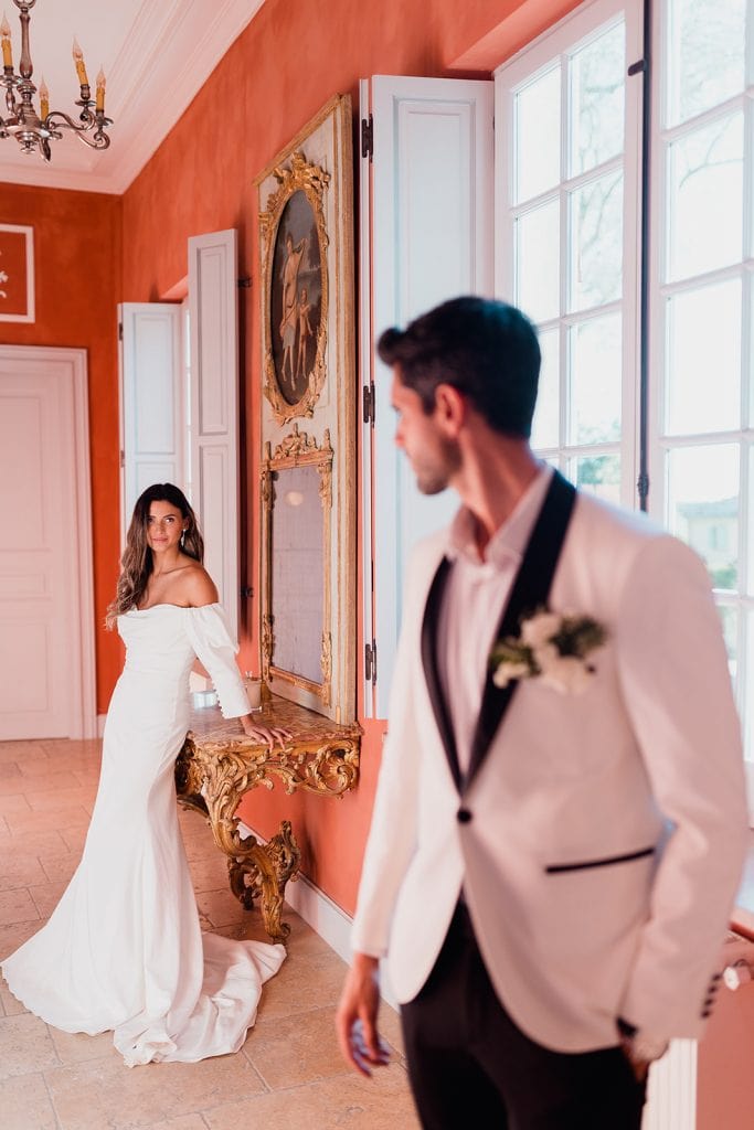 Ornate hallway portrait at Château Beauregard – Maxime Bernadin Bride in an off‑shoulder gown stands in an ornate hallway while the groom gazes from the foreground at Château Beauregard, captured by Maxime Bernadin