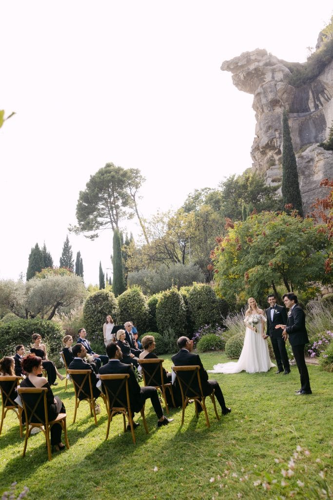 Intimate garden ceremony with guests seated beneath a rocky cliff at L’Étoile des Baux, captured by Maxime Bernadin