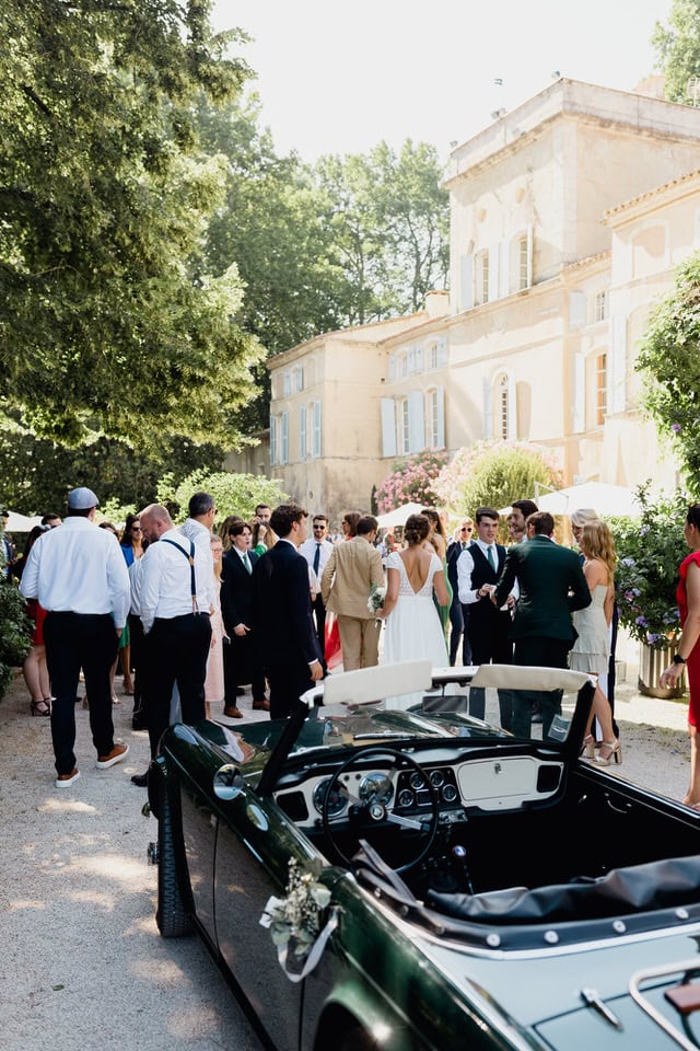 Château reception with classic convertible – Domaine des Barrenques – Maxime Bernadin Wedding guests mingle outside a Provence château with a vintage green convertible car in the foreground at Domaine des Barrenques, captured by Maxime Bernadin