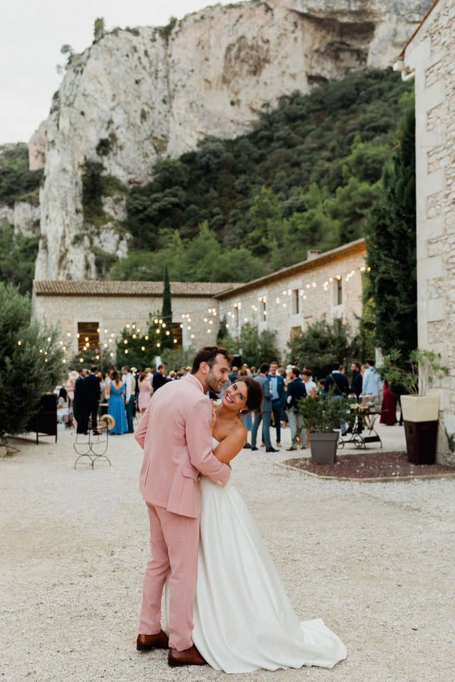 Dancing under the lights at Domaine du Rocher – Maxime Bernadin. Bride and groom dance under string lights in a courtyard bordered by cliffs at Domaine du Rocher, captured by Maxime Bernadin.